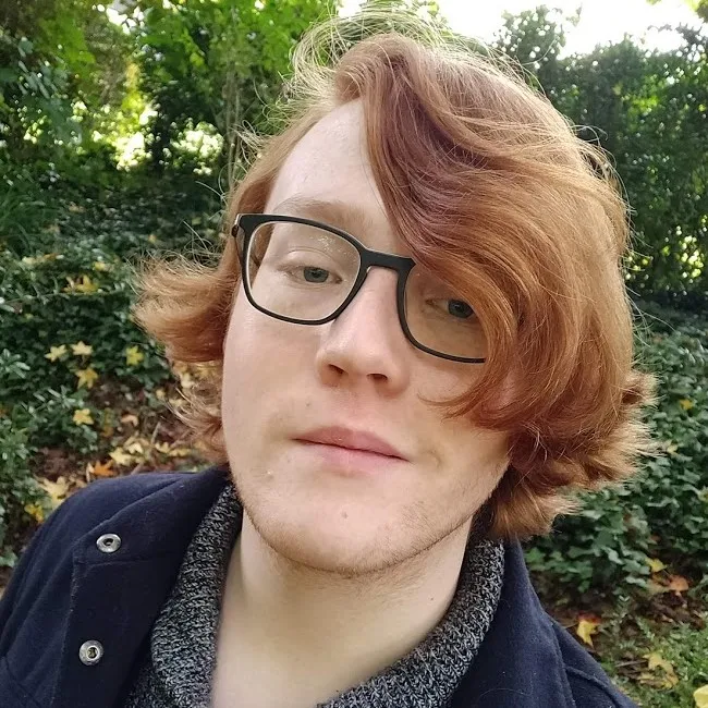 A photo of Felix, who has long red hair and glasses.